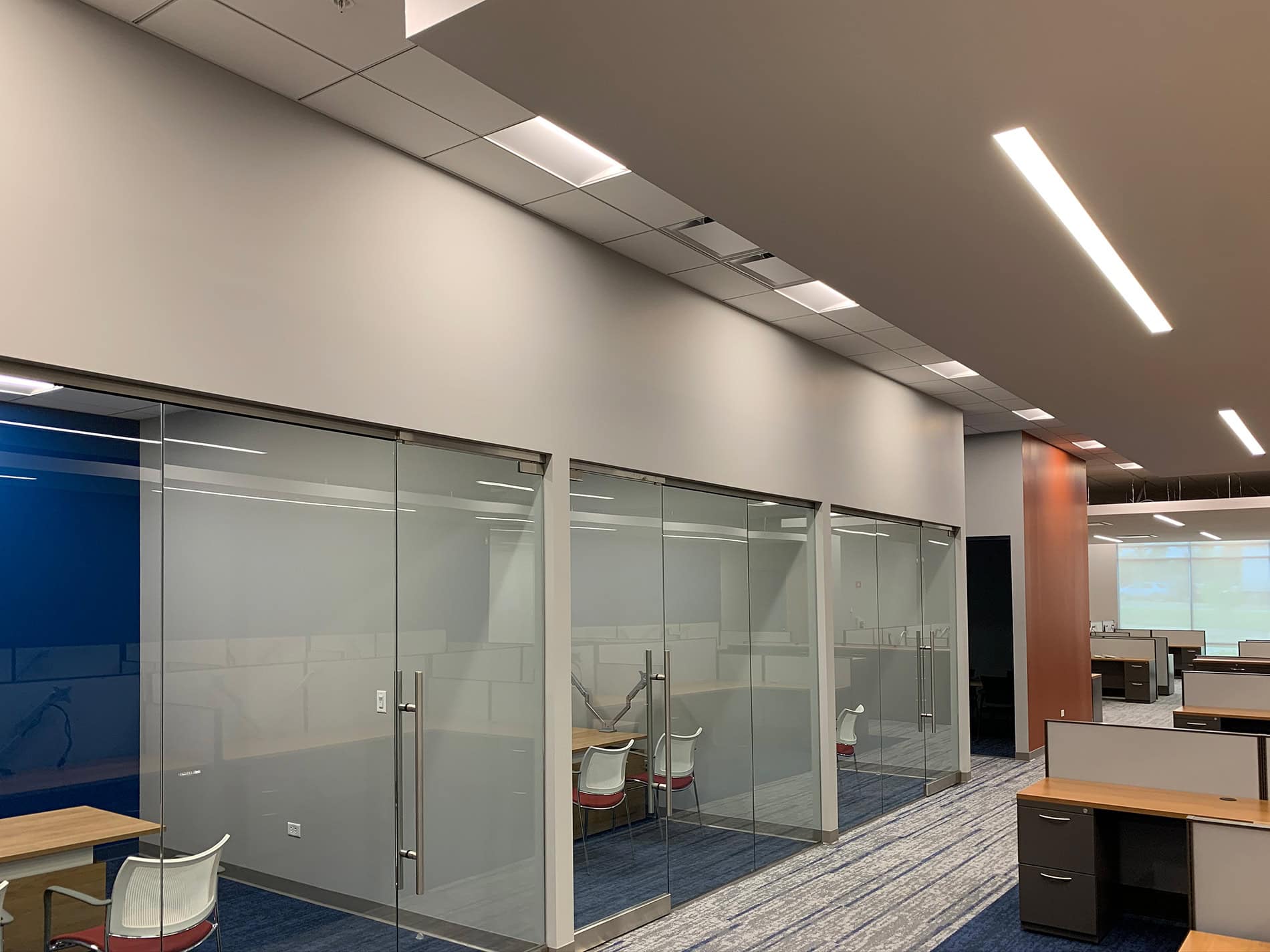 Glass doors into rooms on the left side of a walkway, with low cubicles on the right. These modern upgrades were part of CODA’s renovation done by Keeley Construction, Inc.