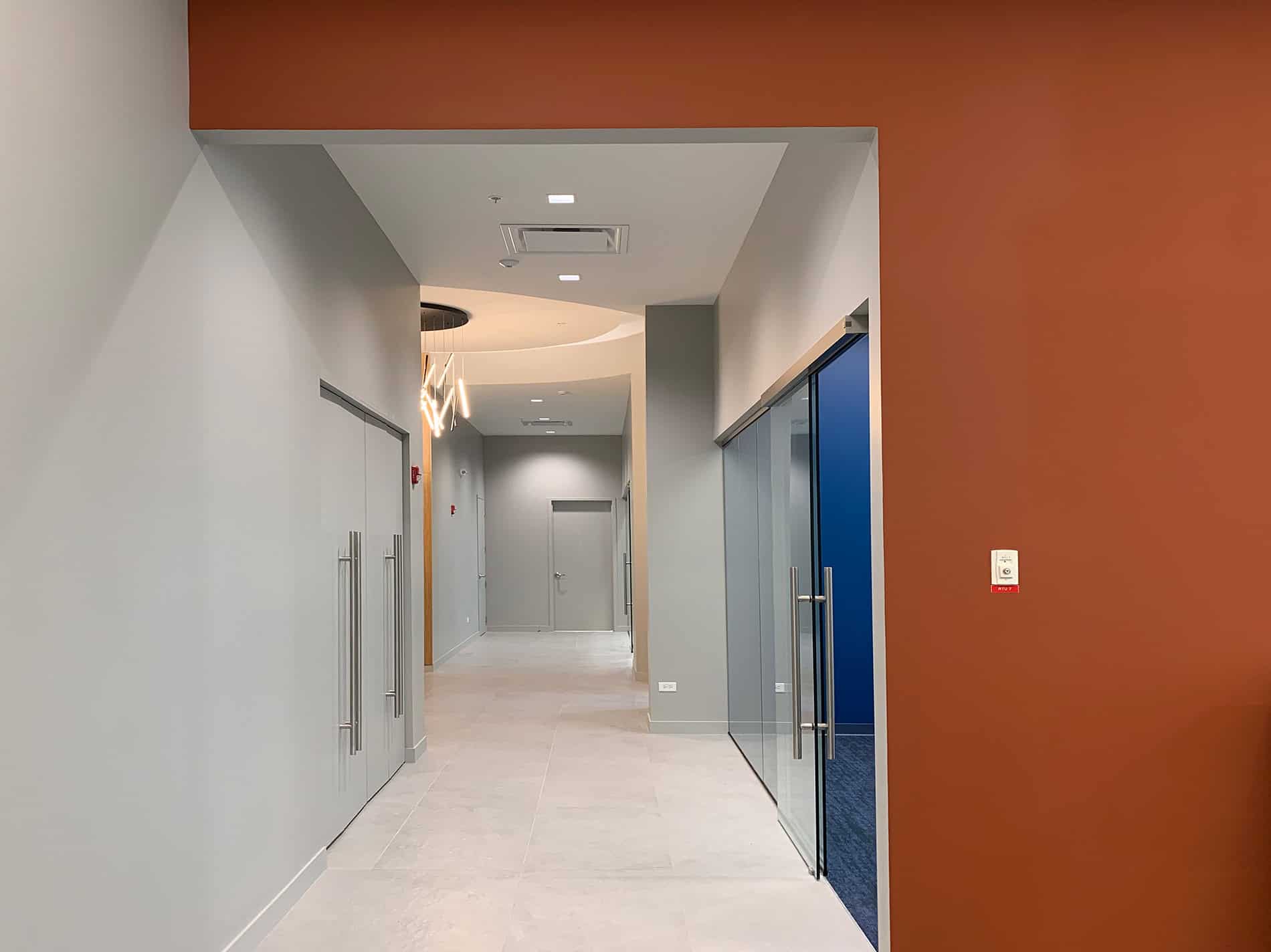 A long hallway has glass walls on the right, and colorful walls.
