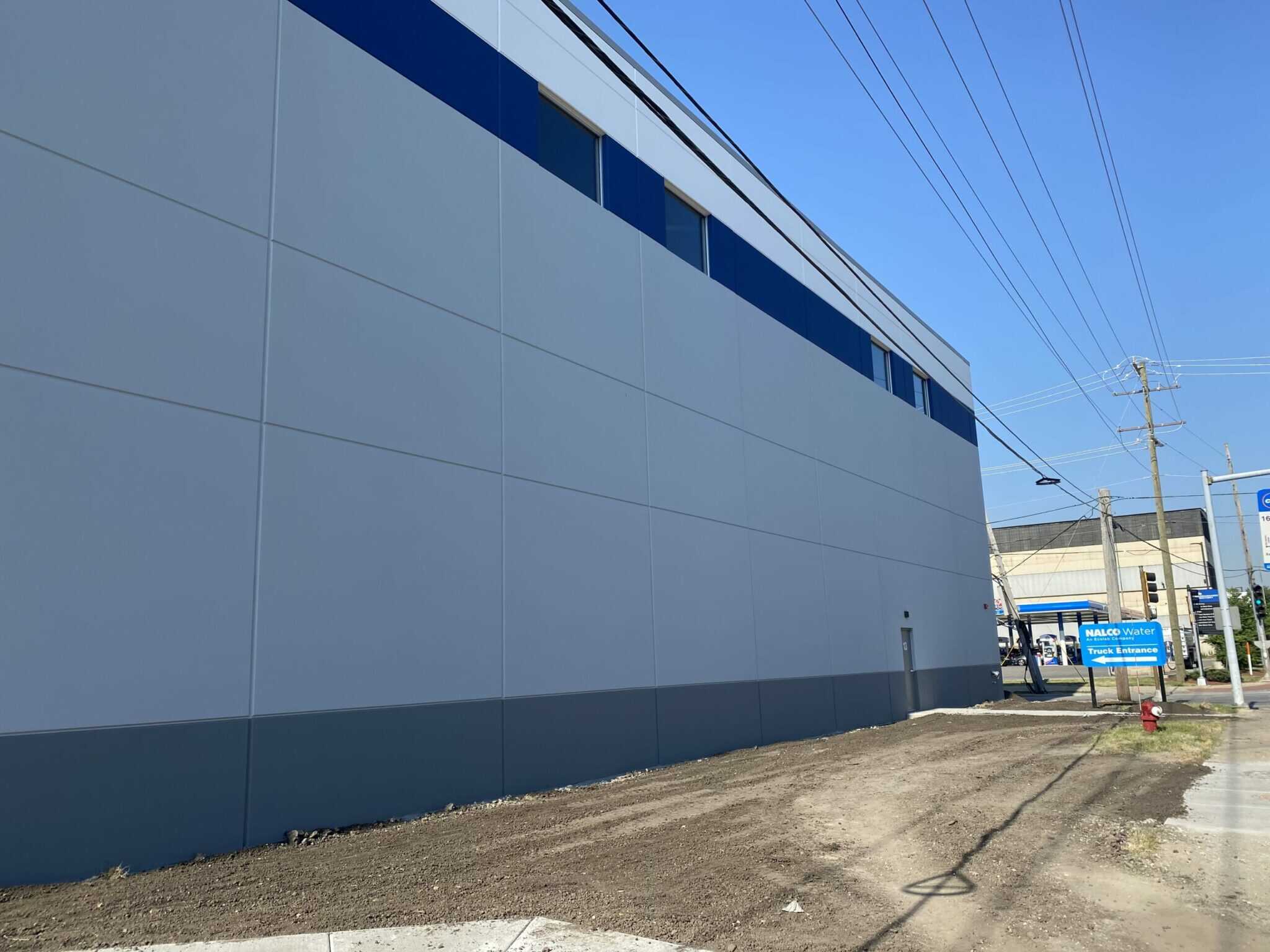 A long outside wall of an industrial building with windows near the top.