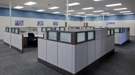 A brightly-lit, open-concept office space full of workspaces with short cubicle walls built for National Technical Systems by Keeley Construction, Inc.