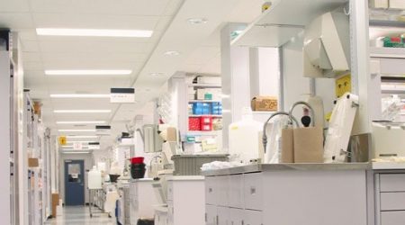 A view down the SGS Life Science’s new laboratory work areas includes rolling carts, eye wash stations, sinks, and high white cubicles with shelves full of science equipment, boxes, and storage space. The interior renovation was completed by Keeley Construction, Inc.