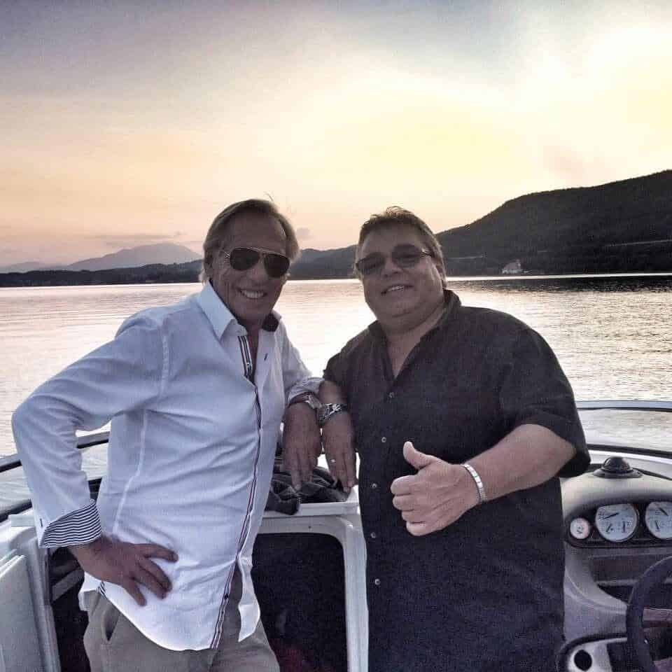 Zwei Männer lachen und posieren auf einem Boot bei Sonnenuntergang, symbolisieren Freundschaft und Z.
