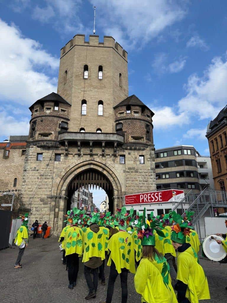 Karnevalsgruppe in bunten Kostümen vor der Kölner Stadtmauer.