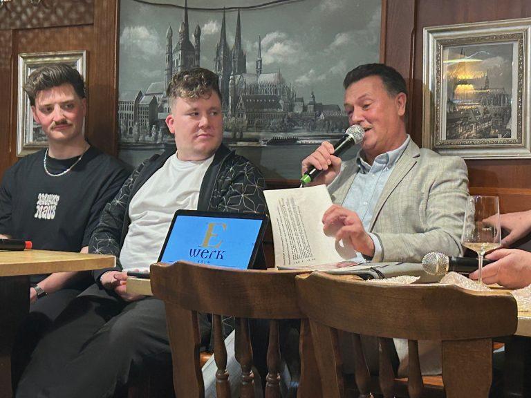 Männer bei Karnevalsveranstaltung diskutieren, einer liest vor.