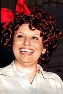 Fröhliche Frau mit roten Locken und rotem Haarband beim Kölner Karneval, strahlend und lebendig.