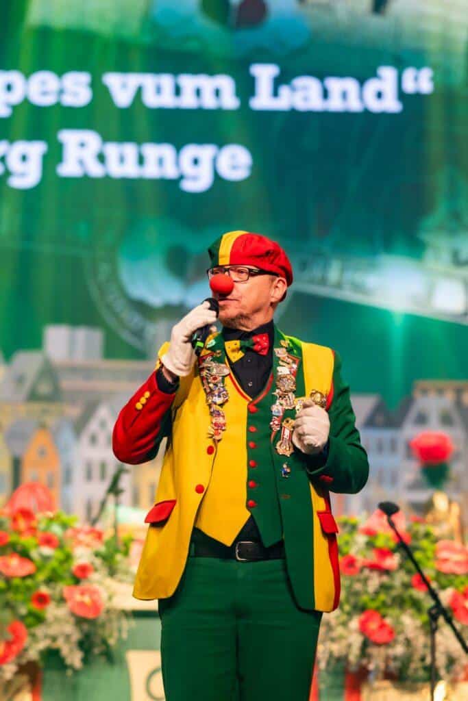 Jubelnder Karnevalsclown in bunter Verkleidung bei Jubiläumsfeier.