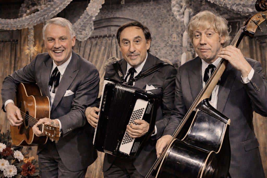 Drei Musiker in Anzügen spielen beim Kölner Karneval mit Gitarre, Akkordeon und Kontrabass.
