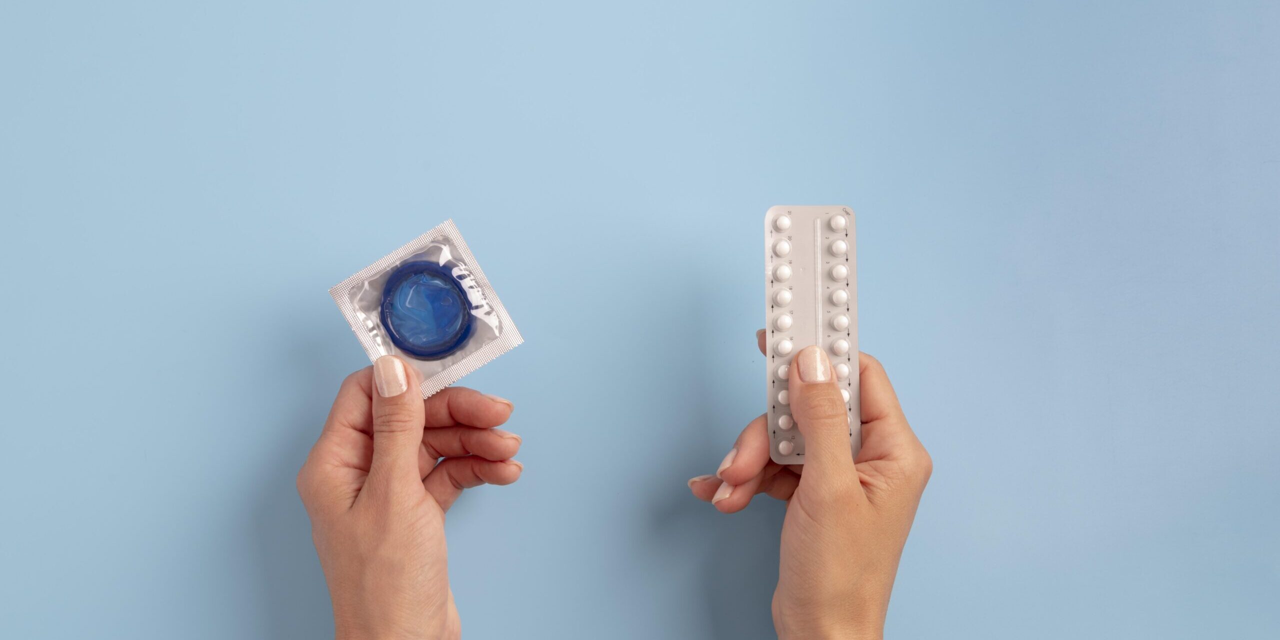 Close-up of hands holding contraceptive options – condom and pills