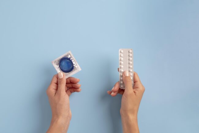 Close-up of hands holding contraceptive options – condom and pills