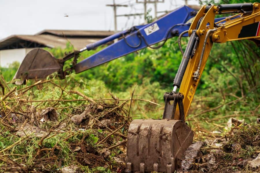 Excavator clearing vegetation and debris during a professional land clearing process.