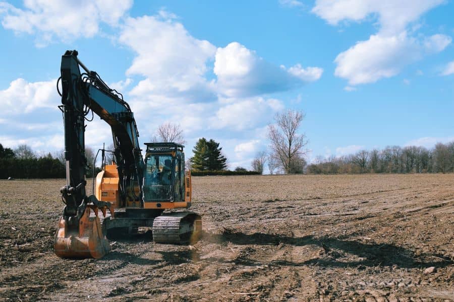 Excavator levelling soil in an open field during environmentally responsible land clearing.