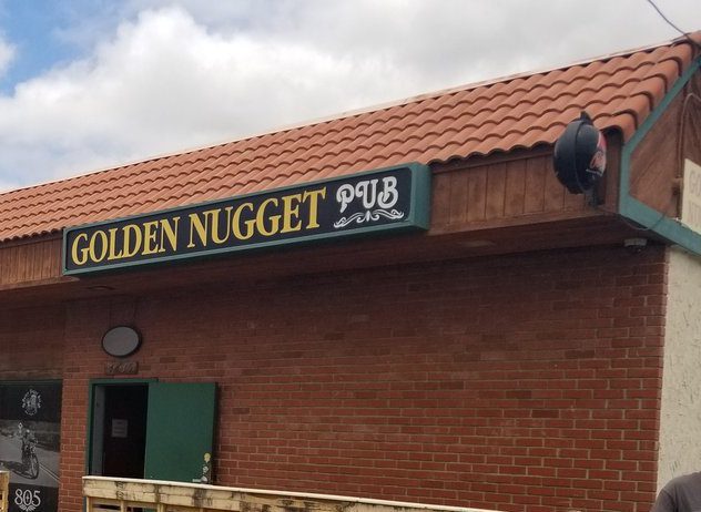 Brick building with a sign that reads Golden Nugget Pub in yellow and white letters. The door is slightly ajar.