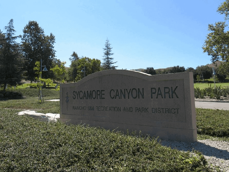Sycamore Canyon Park sign with bushes around it and trees in the background