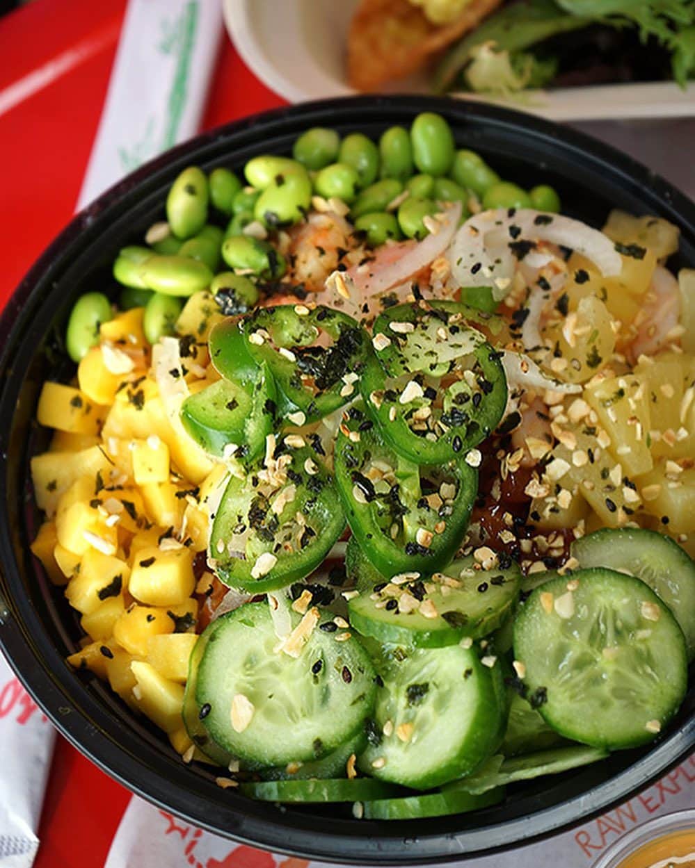A bowl of poke with cucumber, jalapeño slices, edamame, diced pineapple, onions, and sprinkled with sesame seeds.