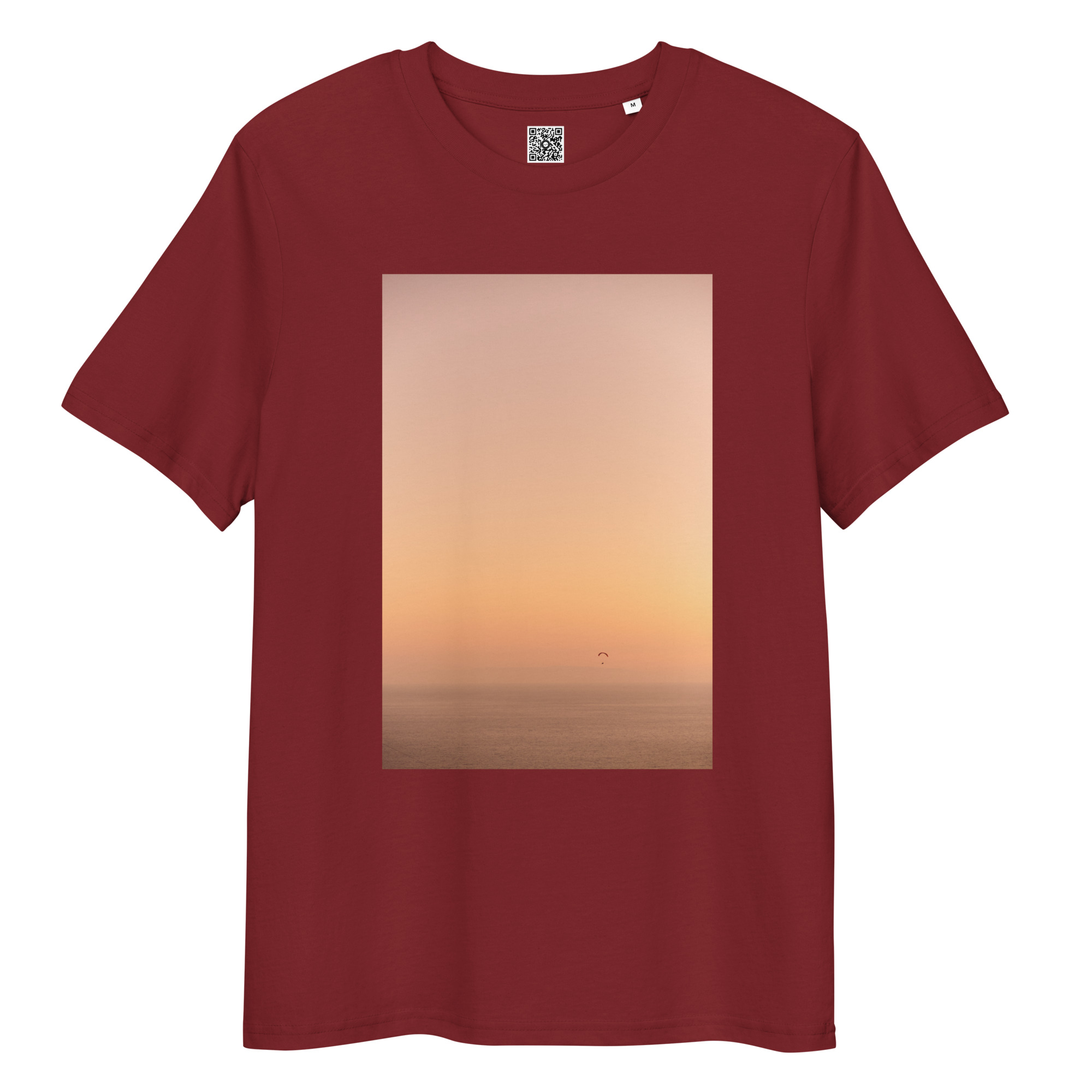 La camiseta unisex de color óxido Parapente al Atardecer muestra una serena puesta de sol sobre el océano con un cielo naranja a rosado y una silueta de una persona en parapente sobre el horizonte.