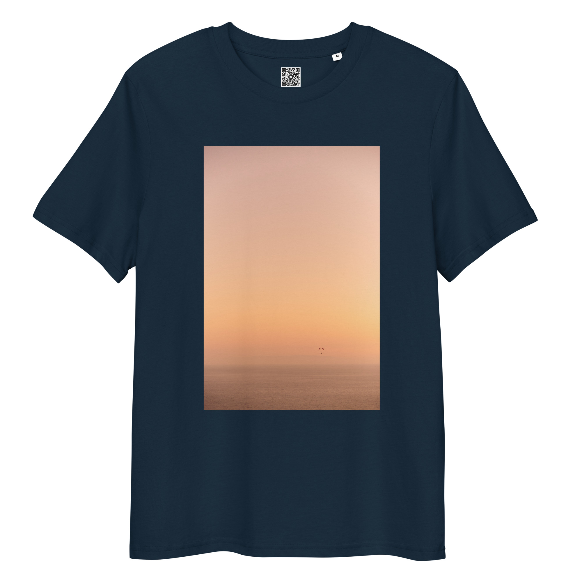 La camiseta unisex Parapente al Atardecer presenta una gran imagen rectangular de un tranquilo atardecer en el océano, con suaves tonos naranjas y rosados. Una silueta de parapente cerca del horizonte captura la esencia del parapente al atardecer.