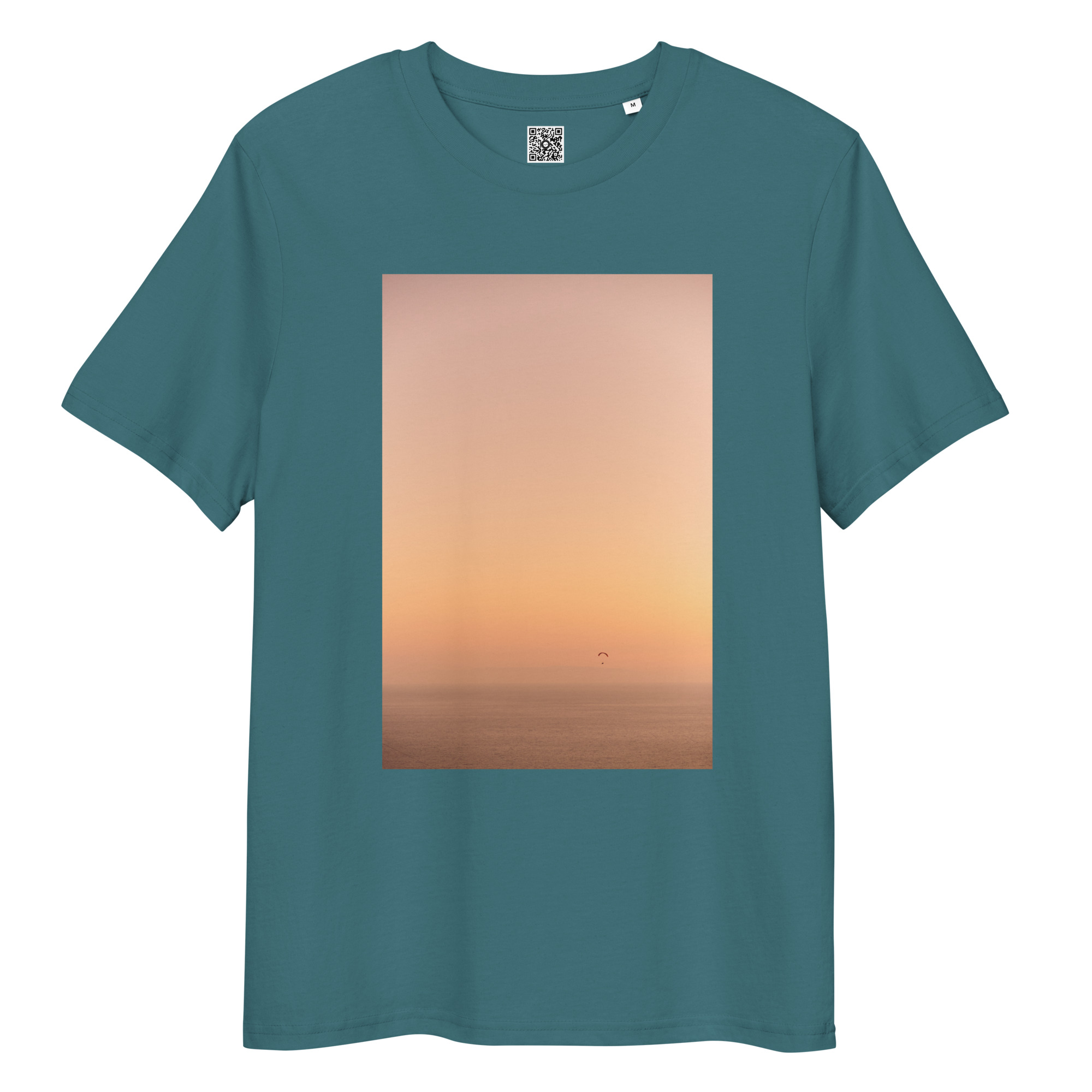 La camiseta unisex Parapente al Atardecer presenta un gran gráfico rectangular en verde azulado, que representa una serena puesta de sol en el océano con una silueta de parapente deslizándose por el cielo nocturno.