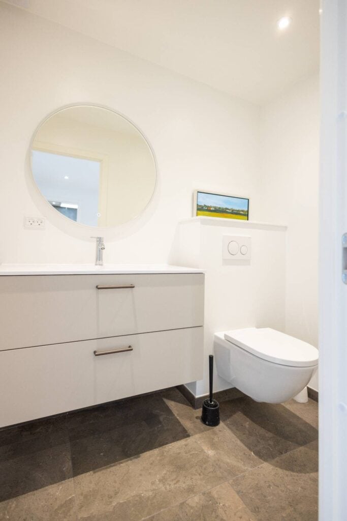 Billig renovering af badeværelse med minimalistisk hvidt vaskemøbel og rundt spejl