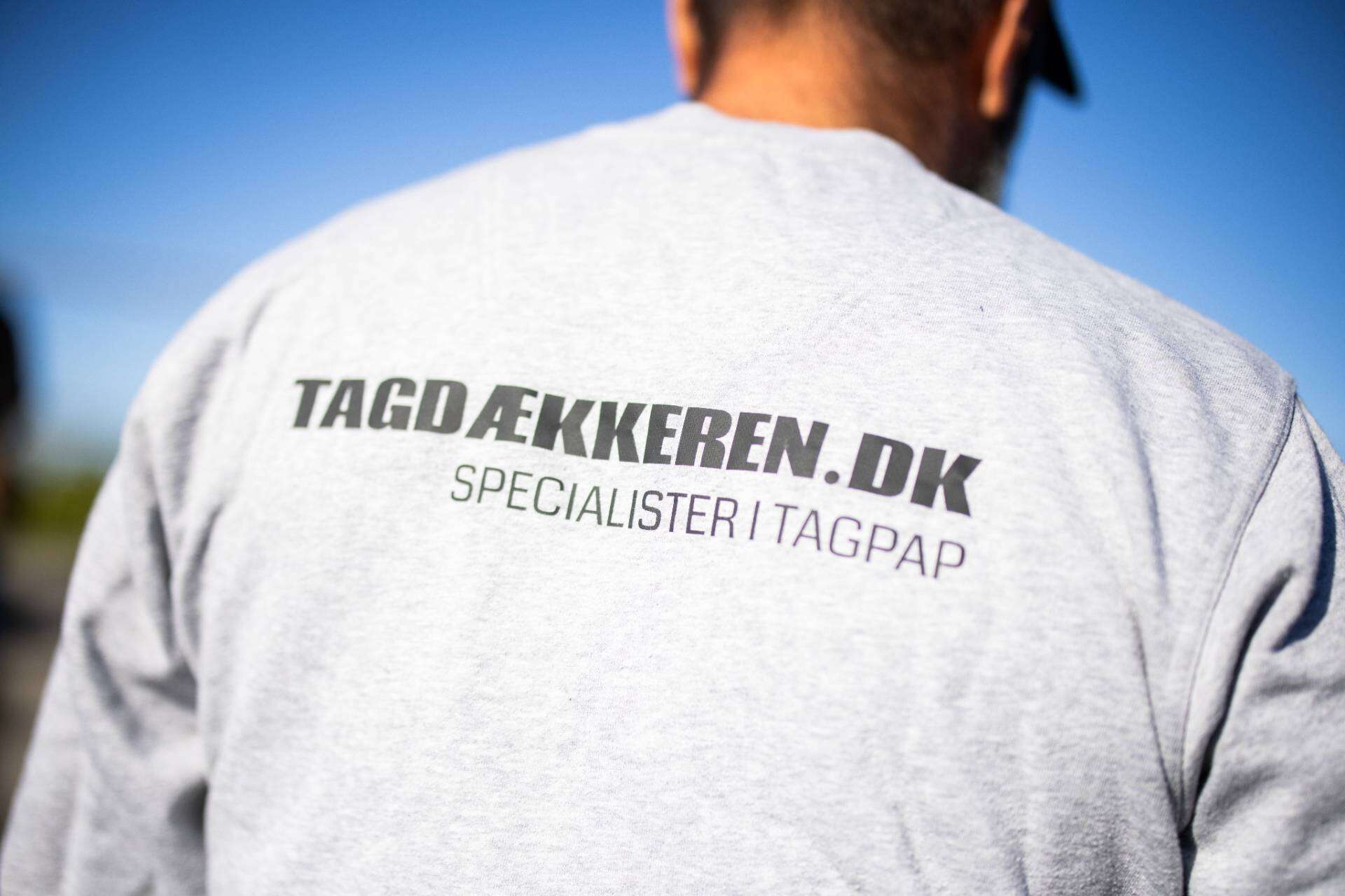 En tagdækker med ryggen til, man kan læse "tagdækkeren.dk" på ryggen