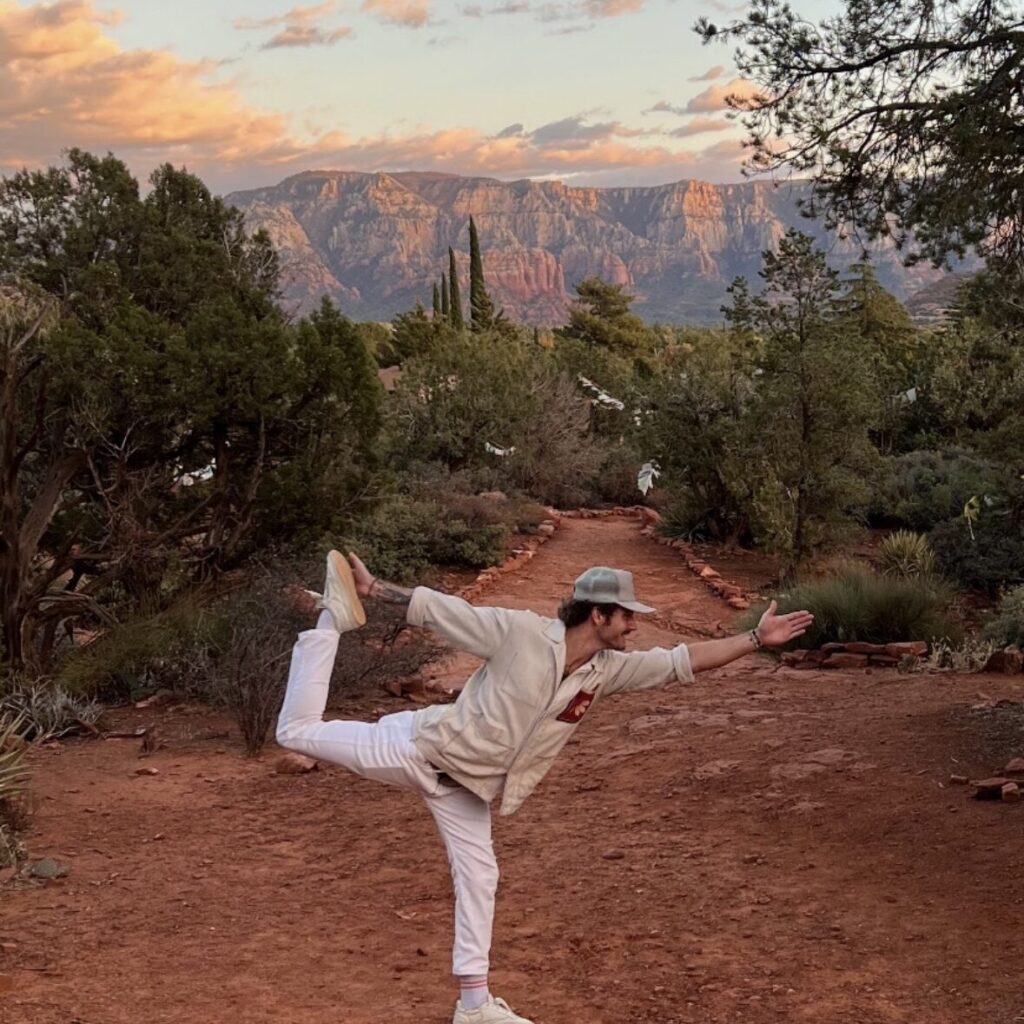 Person doing a yoga pose on a dirt path with trees and distant mountains in the background.