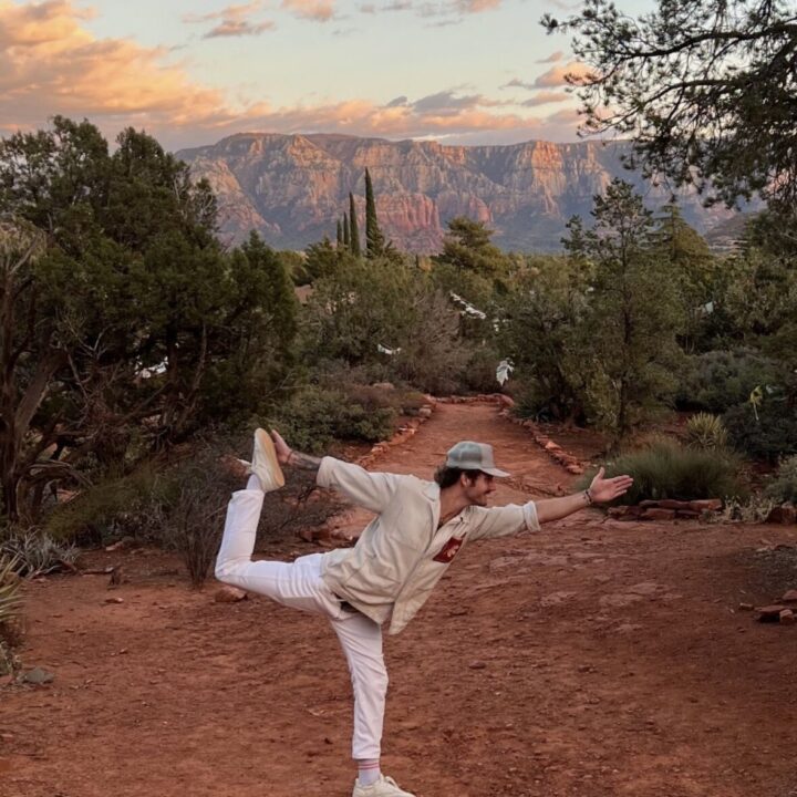 Person doing a yoga pose on a dirt path with trees and distant mountains in the background.