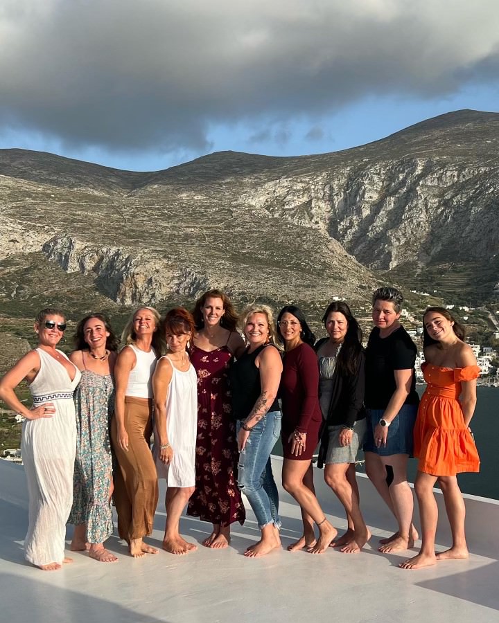 Group of women standing on a white surface with a mountainous landscape and sea in the background.