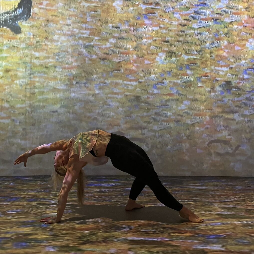 Person performing a backbend yoga pose on a floor with a colorful, projected art pattern.