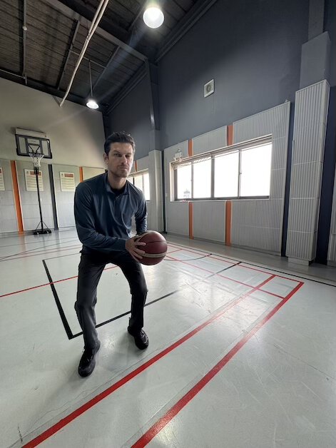 Coach demonstrating basketball stance for youth training at indoor gym.