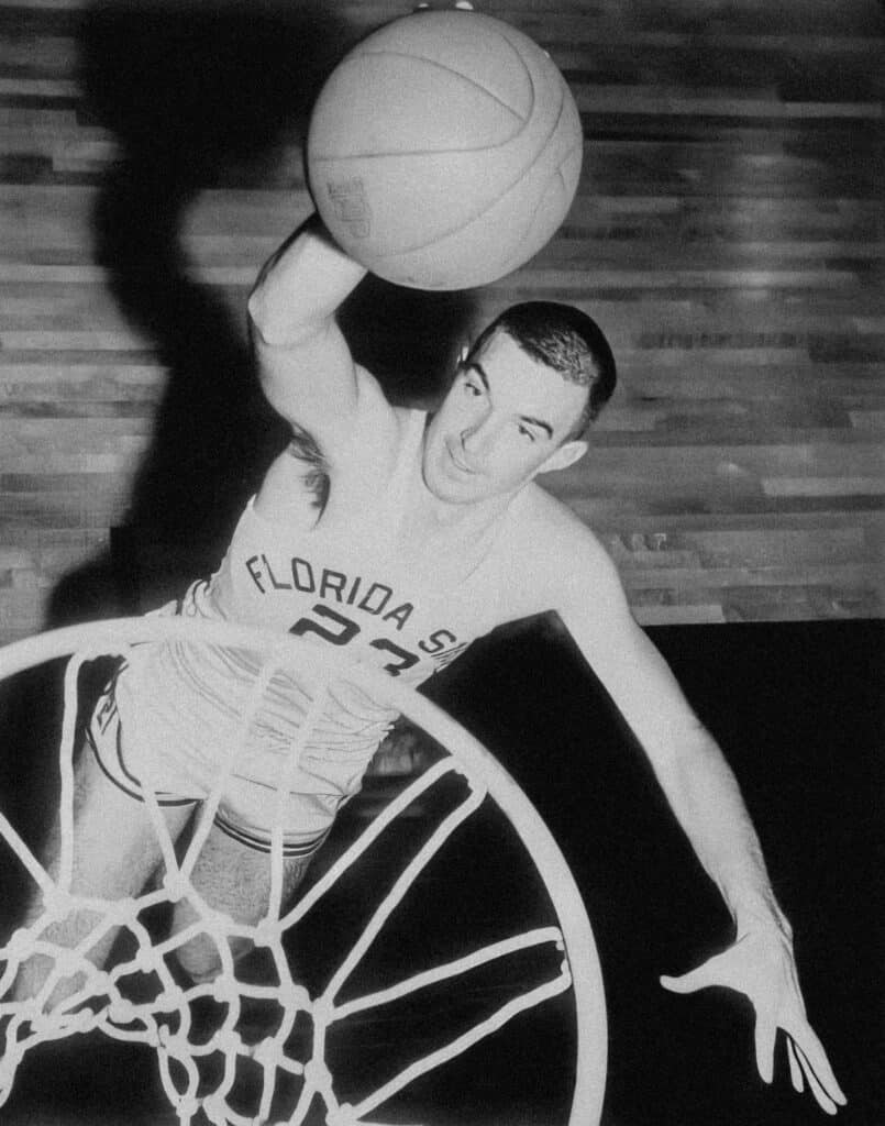 Young basketball player in motion with ball, dunking towards hoop.
