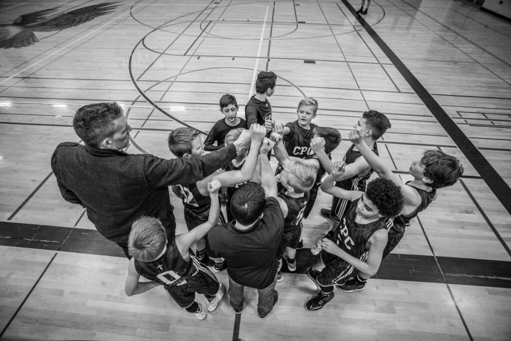 Young basketball players and coach in a team huddle on indoor court.