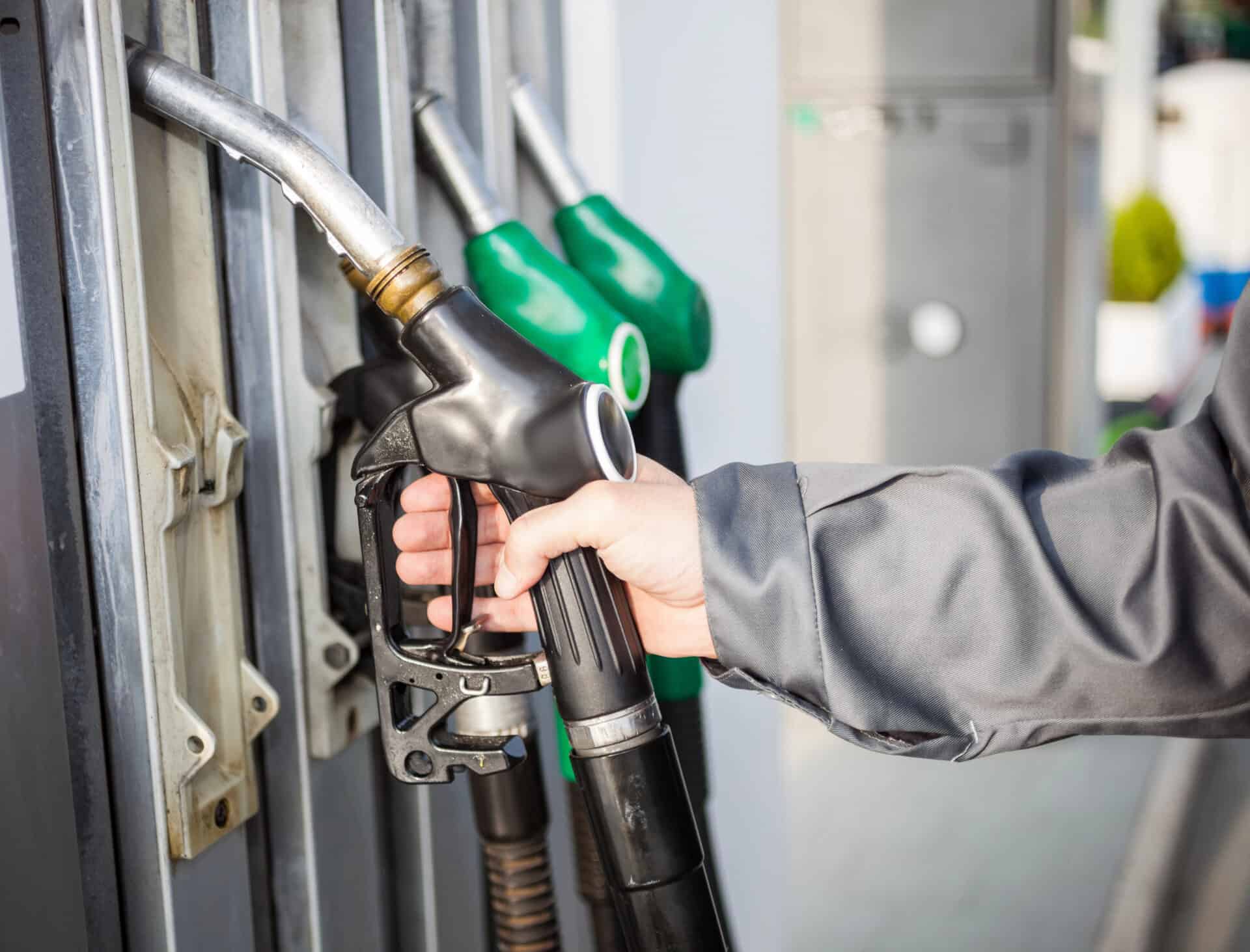 Person refueling vehicle at gas station with fuel pump and nozzles.