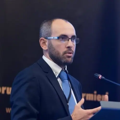 Man in suit speaking at Agro Monitoring conference with microphone.