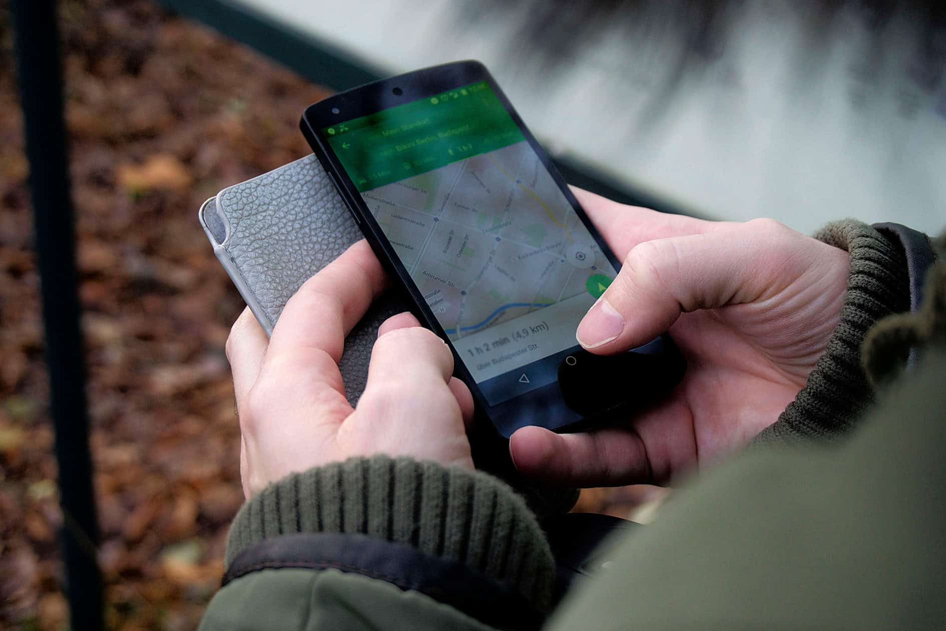 Person using smartphone for agricultural equipment monitoring with GPS map.