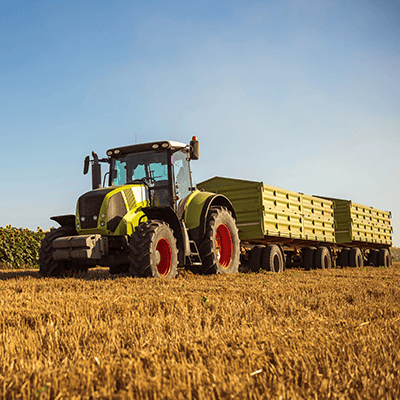 Green tractor hauling hay bales in a field during sunny day.