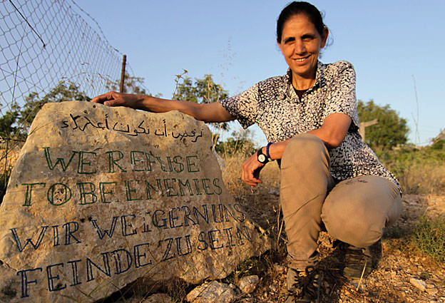 Woman with protest sign in an outdoor setting, smiling at the camera.