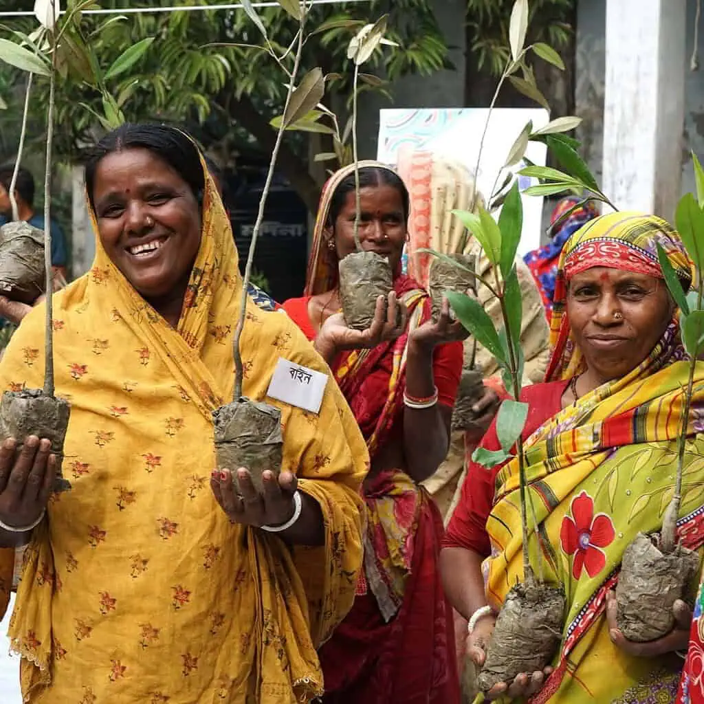 Women holding saplings and clay pots at eco-friendly event in Bangladesh.