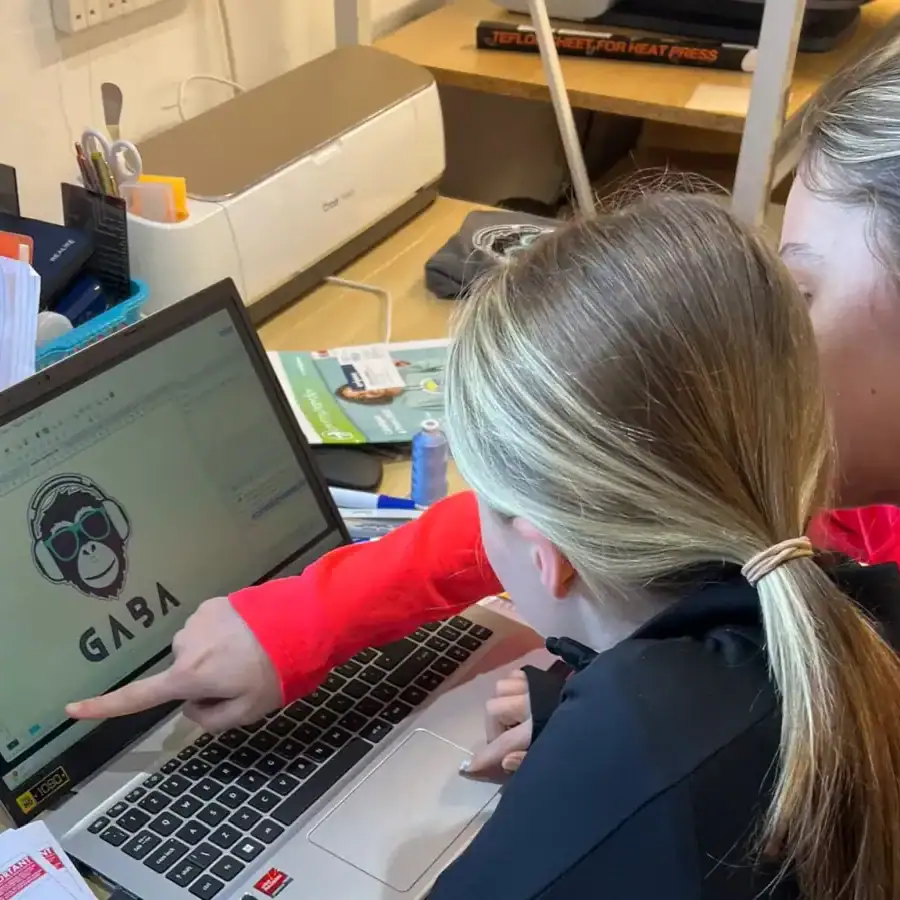 Two women working on a laptop with GABA Clothing logo on screen, in a creative workspace.