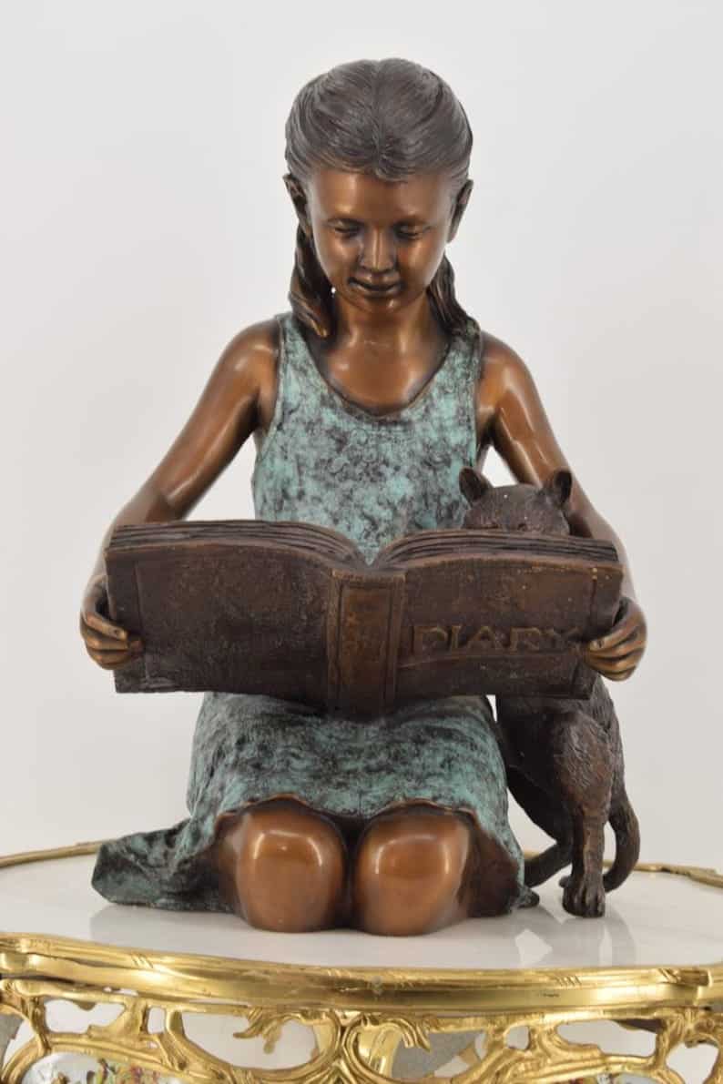 bronze sculpture of girl reading a book to her cat