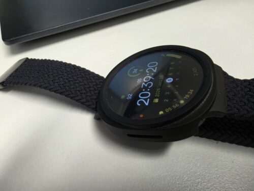 שעון Galaxy Watch 8 עם כיסוי מגן מחוספס עמיד במים, מראה את תצוגת המסך והחוגה, על משטח לבן ליד מחשב נייד.