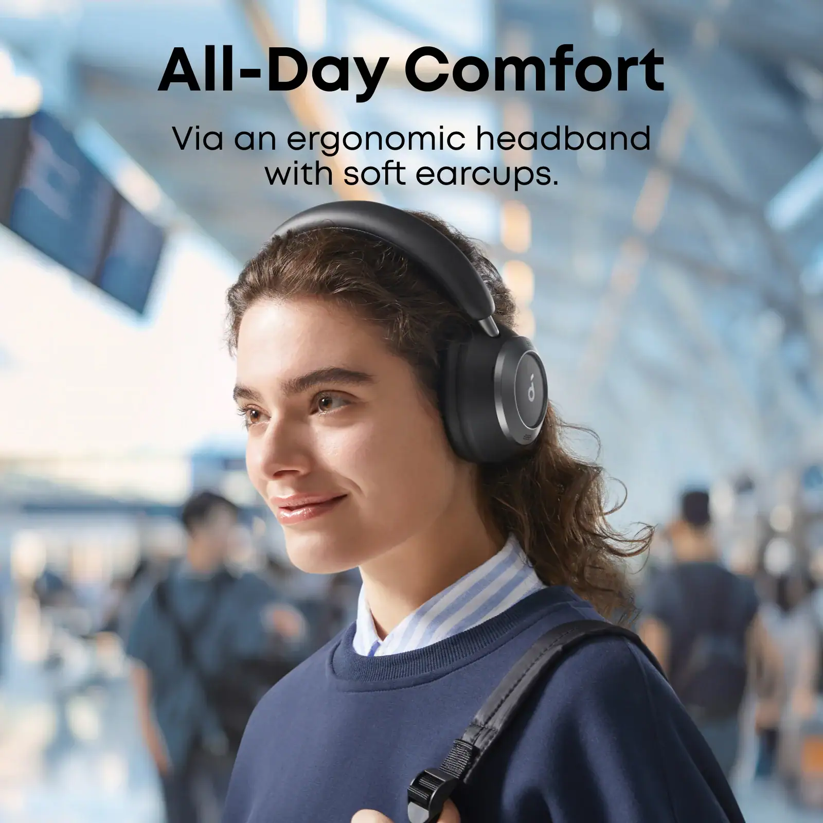 אישה עם אוזניות קשת אלחוטיות Bluetooth נוחות ליום יום, עם ביטול רעשים, באולם תעופה עמוס.