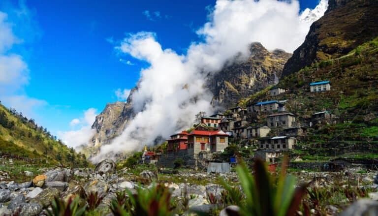 Charming mountain village with traditional houses in a lush green valley under blue sky and clouds near Himalayan peaks.