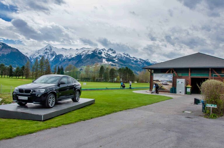 Golfrejser i Tyskland. ZELL AM SEE, Luxury BMW X6 på pedestal i Golfclub Kaprun Zell am See. Black BMW on green of golf course with Alps in background