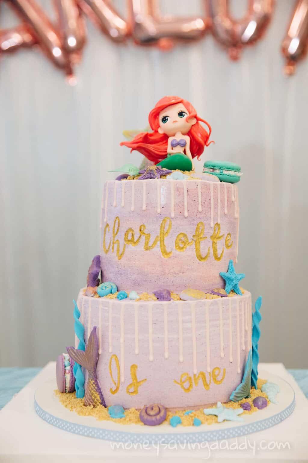 A colorful mermaid-themed birthday cake with "Charlotte" and "It's one" written on it, decorated wit.