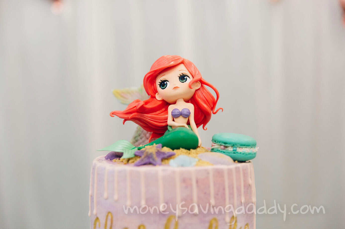Cute mermaid doll figurine with colorful macarons on a pastel cake, decorative and whimsical.