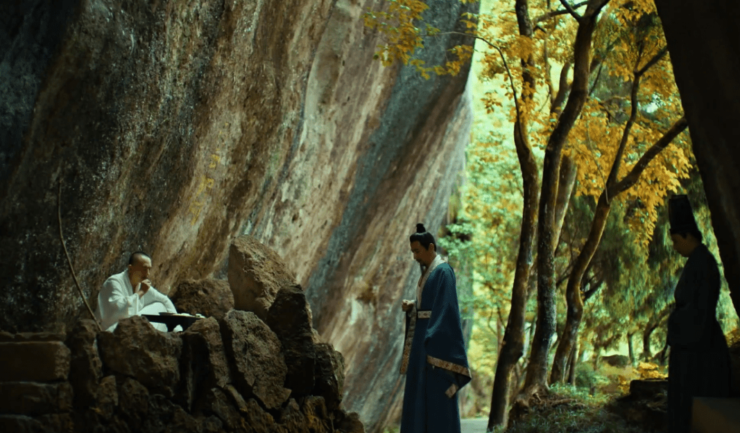 Depiction of Emperor Xiao Yan meeting Bodhidharma in a serene forest setting, with Bodhidharma sitting among rocks and Xiao Yan standing humbly nearby.