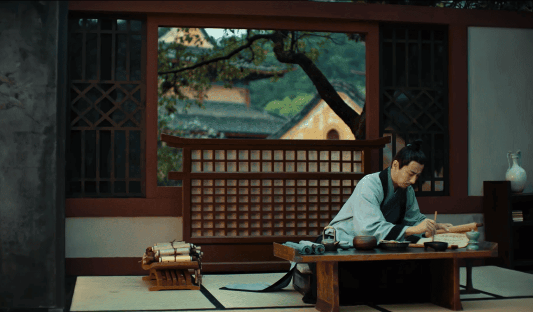 Emperor Xiao Yan seated at a desk, engrossed in writing, representing his scholarly pursuits in a serene, traditional setting.