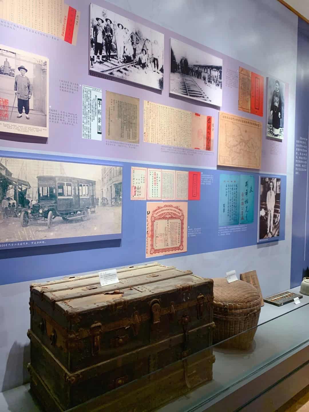 A display at Haikou Port Silver Letter Museum in Taishan featuring vintage photographs, documents, and artifacts like a wooden chest and woven basket.