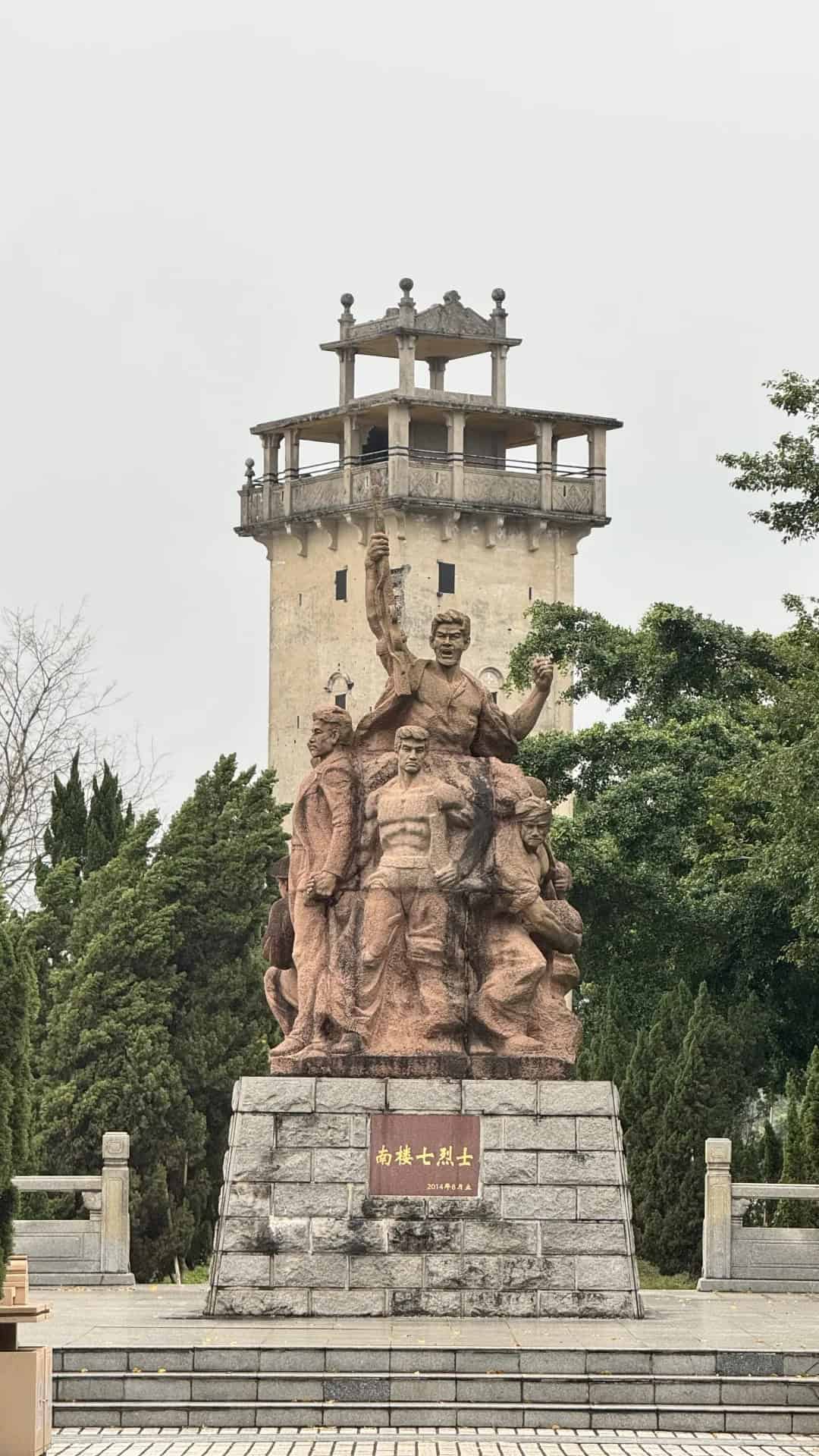 The Seven Martyrs Monument in Nanlou, Kaiping, featuring a group of figures on a stone pedestal with a traditional diaolou watchtower in the background.