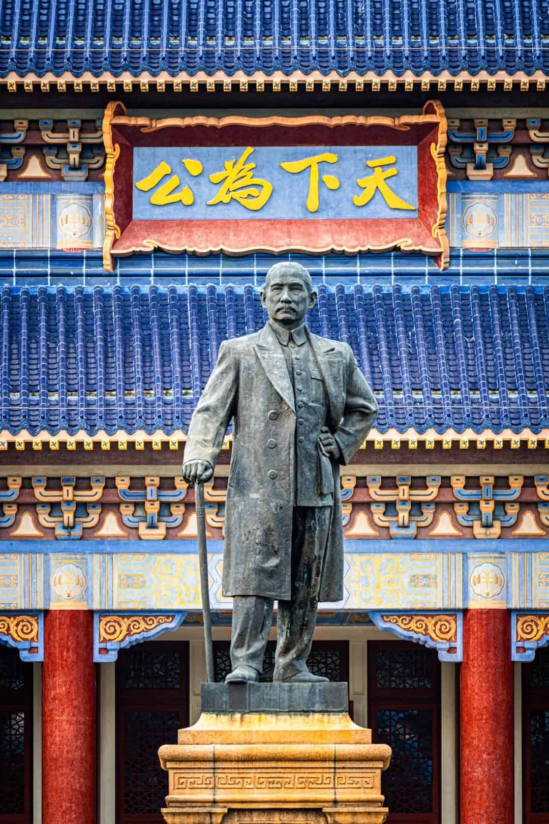 A statue of Sun Yat-sen in Zhongshan stands in front of a traditional Chinese building with blue tiles, red pillars, and a sign reading "孙中山."