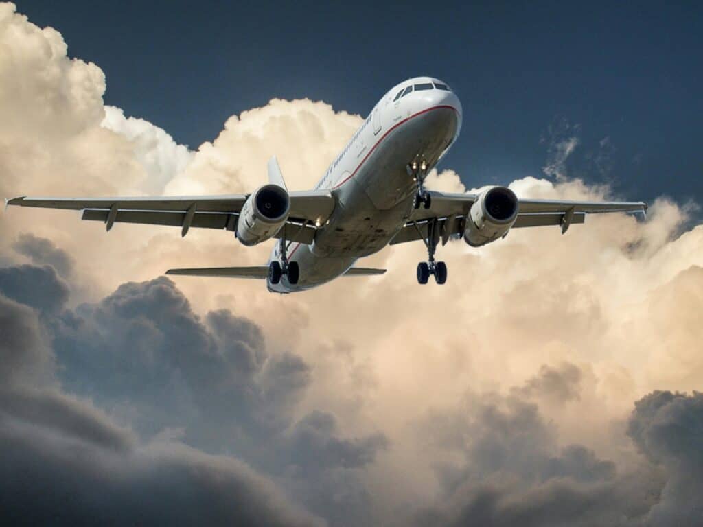 A commercial airplane flying through the sky with dramatic clouds in the background, representing air travel and global transportation.
